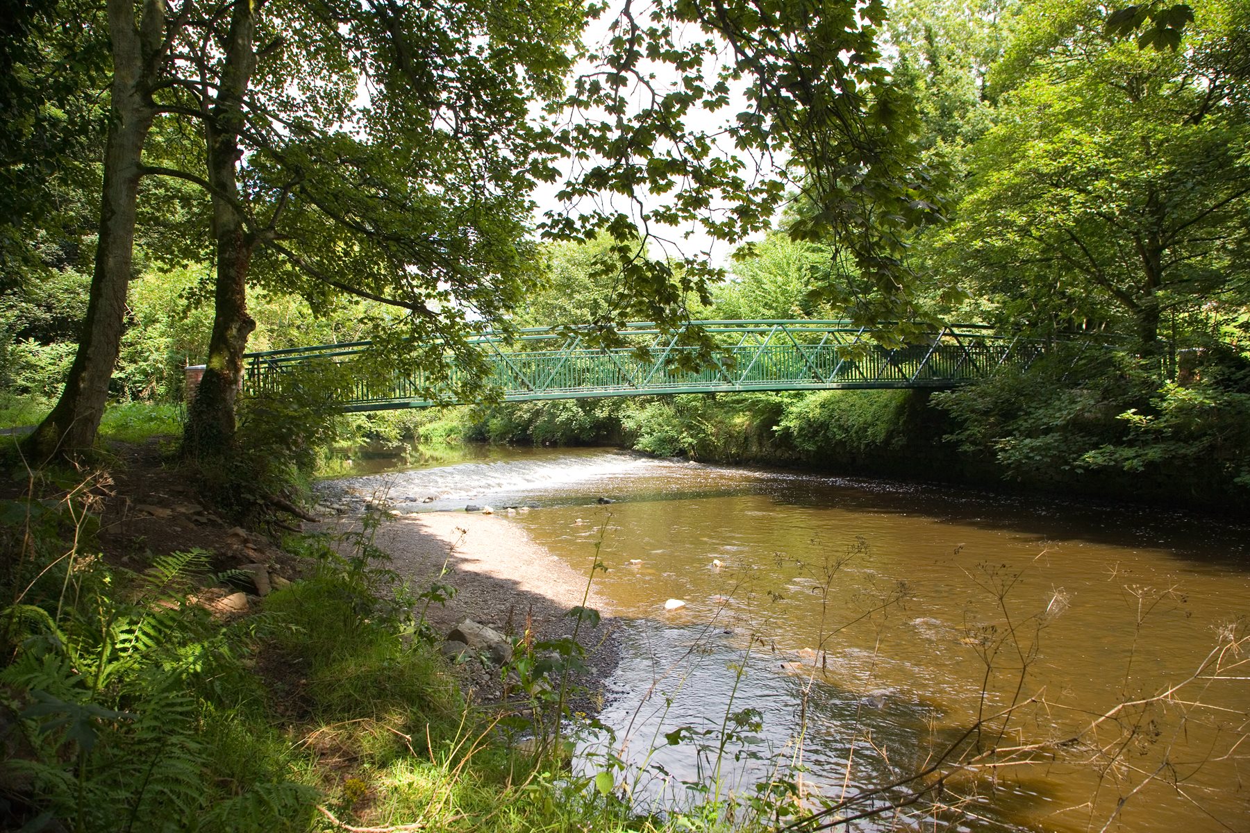 Six Mile Water Park in Ballyclare, Northern Ireland, showing a wide, calm river flowing between lush green banks and mature trees under a clear sky.
